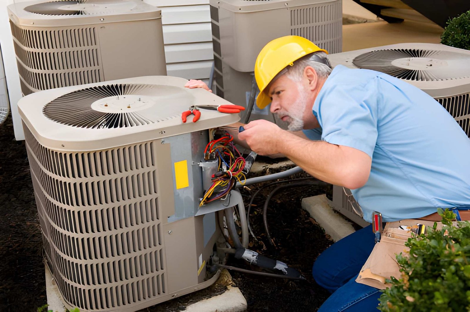 Technician in a hard hat repairing wiring on an outdoor unit